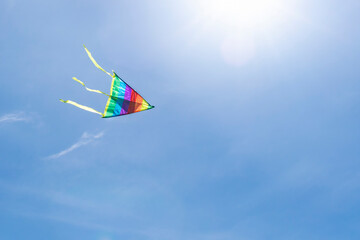 The multi-colored strips of a rainbow kite flies in the clear blue sky in the rays of the sun. The concept of a dream, freedom, childhood, happiness, success. Background with copy space.