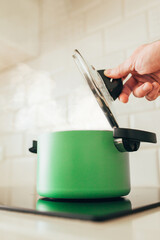 The hand opens the lid of the pot boiling on the stove - cooking the first course of the soup - steam from under the pan lid