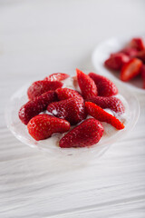 Strawberry dessert in a plate with ice cream and cream on a white wooden background