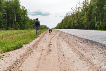 young man, a teenager with a dog is walking on the side of the road. view back