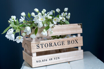 Wooden box for storing things with the inscription Sweet home with an apple flowering branch on a white vintage stool against a dark blue wall.