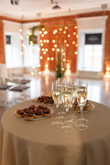 Reserved table with various snacks at the welcome party. Canape and sandwiches, champagne. Interior decorated with garlands.