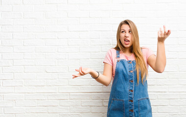 young blonde woman shrugging with a dumb, crazy, confused, puzzled expression, feeling annoyed and...