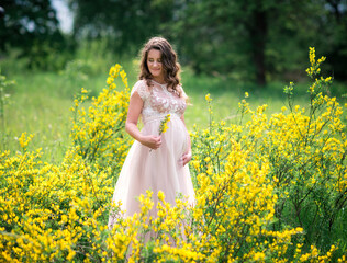 Naklejka na ściany i meble Pregnant happy woman in a beautiful dress in a blooming yellow field outdoors. Beautiful nature, female portrait in wild flowers