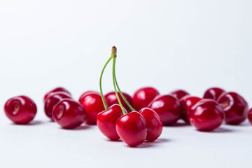 Obraz na płótnie Canvas Three red cherries on one stalk. In the background a lot of red cherries. Red ripe sweet cherries on a white background
