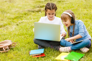 two funny schoolgirls sit on the grass and read books. Girls, girlfriends, sisters are taught lessons in nature.