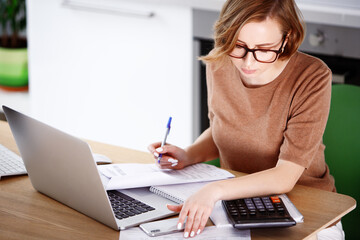 Woman sitting at laptop computer, making notes, calculating expenses, planning family budget, debts...