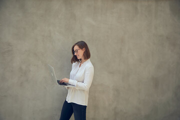 Beautiful business woman standing with her laptop in front of a large concrete wall