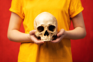 Skull in the hands of young girl. Human skull on an yellow background. Fragment of a human skeleton. Study of the remains. Concept - research into the causes of death.
