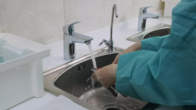 Medium shot of Doctor in white gloves wash dental tools with a brush under a stream of running water from the tap. Before the disinfection procedure of orthodontic pliers.