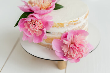White naked cake with pink peonies on the top. Birthday one year old baby girl party decorations. Cream cheese white simple cake