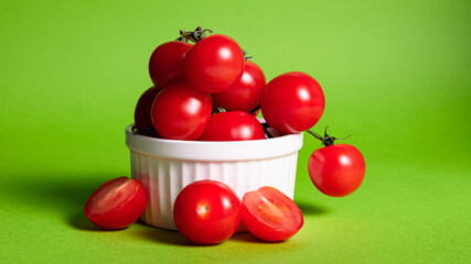branch of cherry tomatoes in a white bowl on a green background, close-up