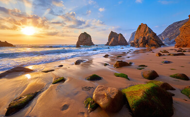 Ursa Beach in Portugal. Atlantic coast of Atlantic Ocean. Sunset and rocks sun waves and foam at sand of coastline picturesque landscape panorama.