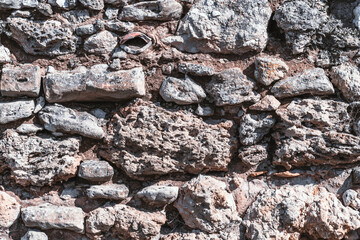 The texture of the wall of stones of different sizes, limestone, and shell rocks, concrete, and cement layers, shards of metal and bricks with clay and twigs in seams
