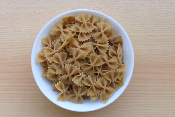 Uncooked Italian noodle farfalle, also known as bow-tie pasta or butterfly pasta, in a white bowl, from above