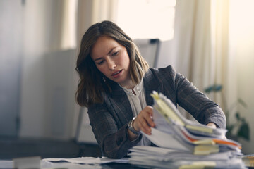 Busy business woman looking through a large pile of paperwork on her office desk, being stressed.