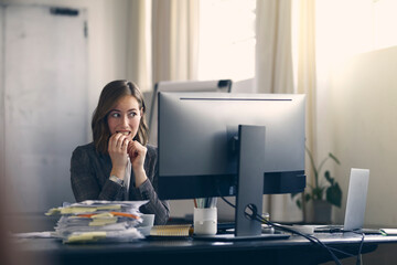 Business woman biting nails in suspense while looking at her computer. Modern office space. 