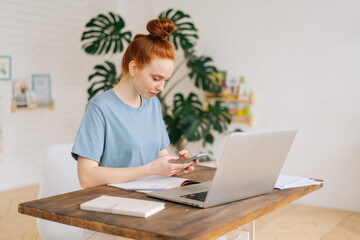 Millennial redhead young businesswoman browsing internet on phone at workplace. Portrait of cute business woman checking cellphone content online at home.