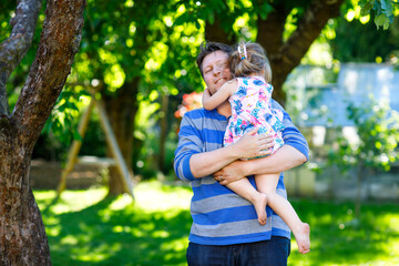 Naklejka premium Happy young father having fun cute toddler daughter, family portrait together. man with beautiful baby girl in summer garden. Dad with little child outdoors, hugging. Love, bonding.