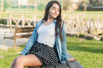 natural beautiful caucasian girl sitting on a wodden bench in the park with her eyes closed.