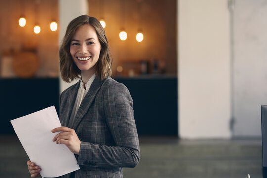 Close up portrait of attractive and professional business woman wearing a suit holding paperwork while giving a big happy smile in camera. 