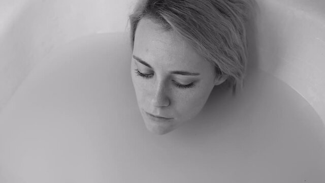 Sad depressed woman submerging under the water in the bathtub at home. Black and white shot