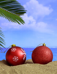 Summer xmas holidays concept. Christmas ornaments on sandy beach with palm tree, blue sea and sky background