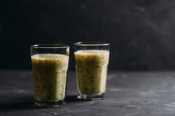 Kiwi and pear smoothies in glasses with a straw on a dark background side view