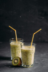 Kiwi and pear smoothies in glasses with a straw on a dark background side view