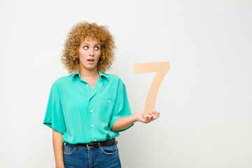 young pretty afro woman surprised, shocked, amazed, holding a number 7.