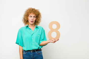 young pretty afro woman surprised, shocked, amazed, holding a number 8.
