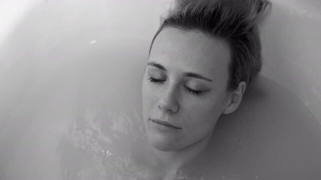 Sad depressed woman submerging under the water in the bathtub at home. Black and white slow motion shot