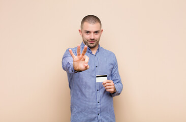 young handsome man smiling and looking friendly, showing number three or third with hand forward,...