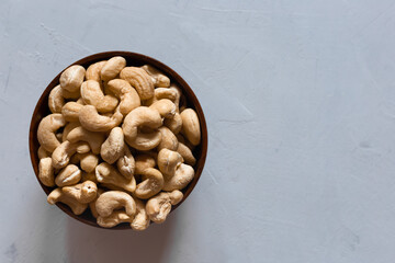 Cashews in a brown wooden bowl on a gray background with a copy of the space. Top view