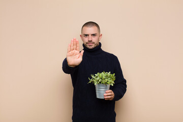young handsome man looking serious, stern, displeased and angry showing open palm making stop...
