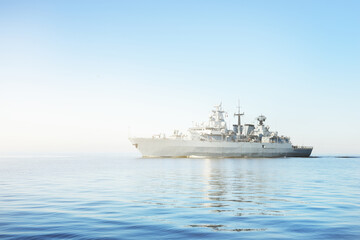 Large grey modern warship sailing in still water. Clear blue sky. Baltic sea, Germany. Global...