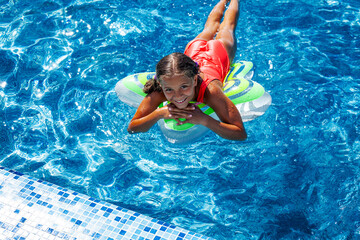 Preteen girl dressed red  swimsuit swimming in the blue resort pool on the inflatanle ring. Summer...