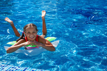 Preteen girl dressed red  swimsuit swimming in the blue resort pool on the inflatanle ring. Summer...