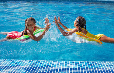 Two tween girls playing, splashing, laughing and have fun in the blue water of swimming pool with inflatanle rings.