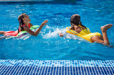 Two tween girls playing, splashing, laughing and have fun in the blue water of swimming pool with inflatanle rings.