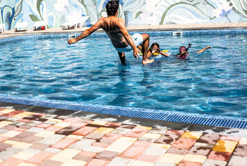 Happiness family,  preteen daughters and father playing , splashing each other with water in the pool. Man jumping to the blue pool