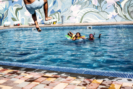 Happiness Family,  Preteen Daughters And Father Playing , Splashing Each Other With Water In The Pool. Man Jumping To The Blue Pool