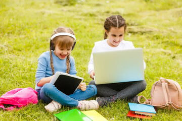 two funny schoolgirls sit on the grass and read books. Girls, girlfriends, sisters are taught lessons in nature.