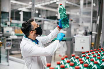 Male worker in workwear and with protective mask on his face working in bottling factory. Inspection quality control.