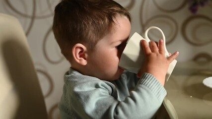 Little child drinks water from a mug on his own. Independent baby
