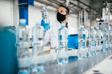 Male worker in workwear and with protective mask on his face working in bottling factory. Inspection quality control.