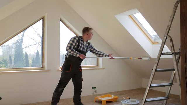 Home improvement concept, handyman painting a wall with a white paint near roof window in attic