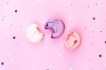 Three bitten macaroon flat lay on pink background with holiday confetti. Birthday party sweet almond dessert. Pink, violet, white colorful wallpaper with space for text. Minimal creative food pattern