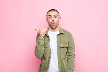 young handsome man looking astonished in disbelief, pointing at object on the side and saying wow,...