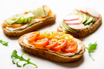 Variety of sandwiches for breakfast, snack, appetizers - avocado, radish, tomatoes, bacon, cucumbers, cream cheese, whole grain bread sandwiches. On a light background.